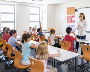 Young female professional teaching boys and girls. Teacher is explaining students in classroom. They are studying in elementary school.