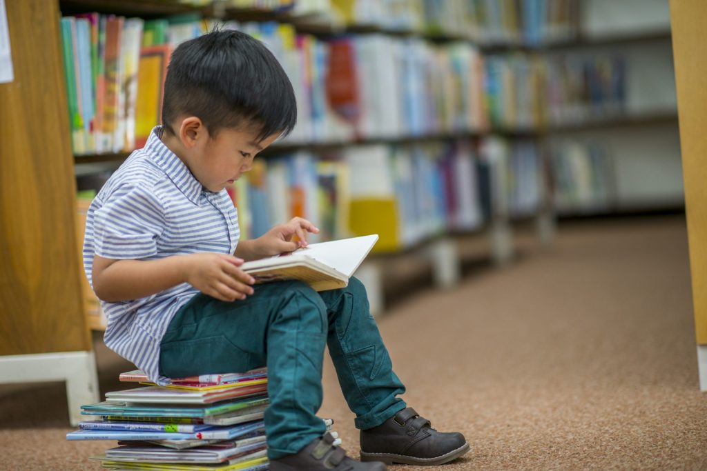 Young boy reading a picture book in the library, building reading fluency and confidence